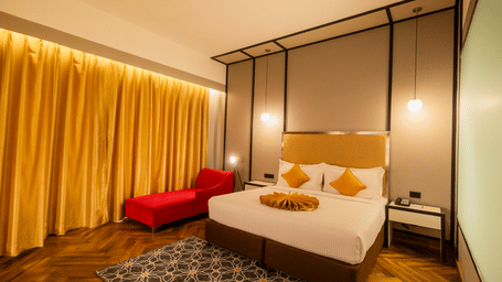 King bed framed by tall canopy, red chaise lounge and golden curtains in a premium guest room at Polo Hotel, Agartala.