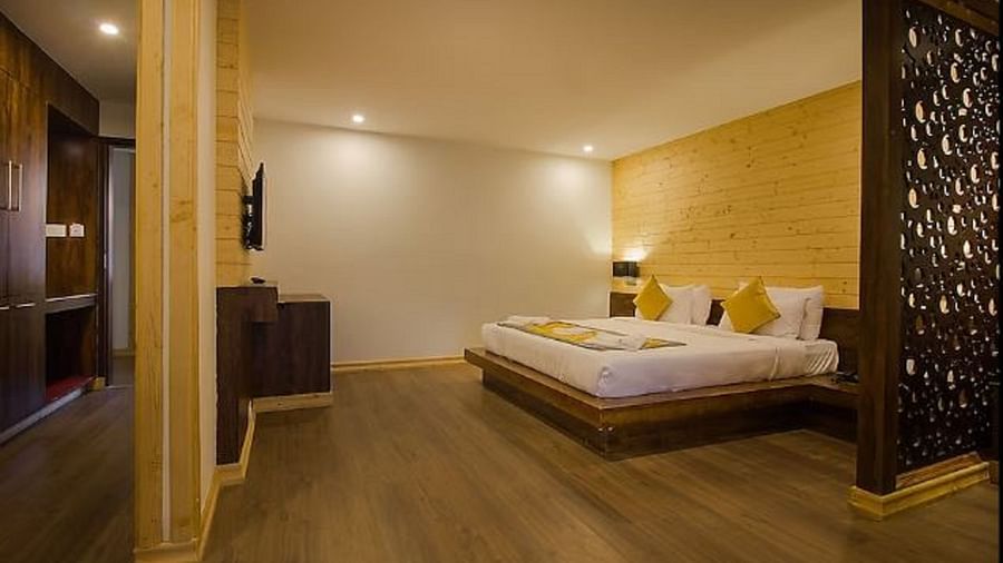 An image of an executive premium room with a bed, flat scree TV, a wooden panelled accent wall behind the bed, and the room is lit with warm lighting - Yashshree Sanderling, Darjeeling