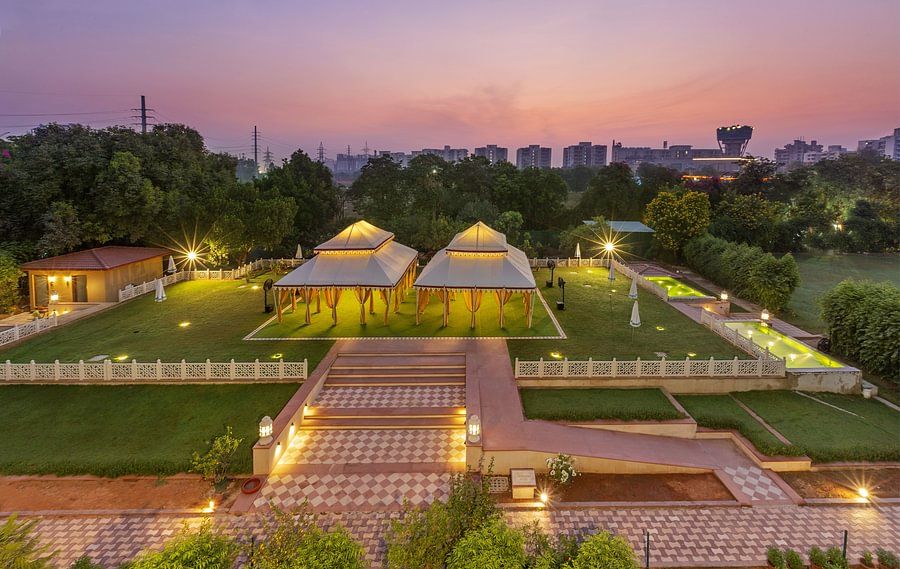 Illuminated tents on a green lawn surrounded by trees under a dusky pink sky - Heritage Village Resorts & Spa.