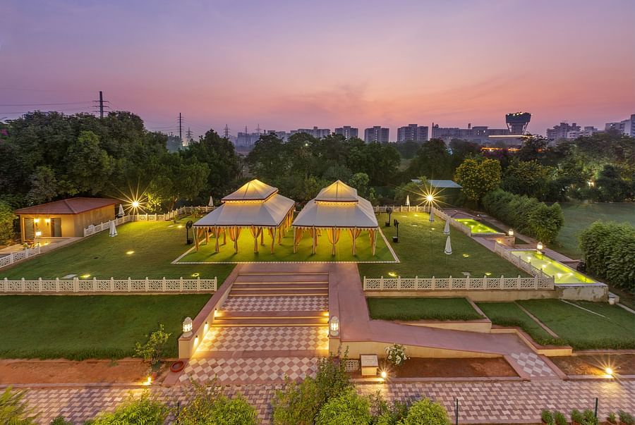 Illuminated tents on a green lawn surrounded by trees under a dusky pink sky - Heritage Village Resorts & Spa.