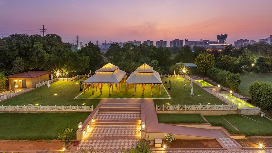 Illuminated tents on a green lawn surrounded by trees under a dusky pink sky - Heritage Village Resorts & Spa.