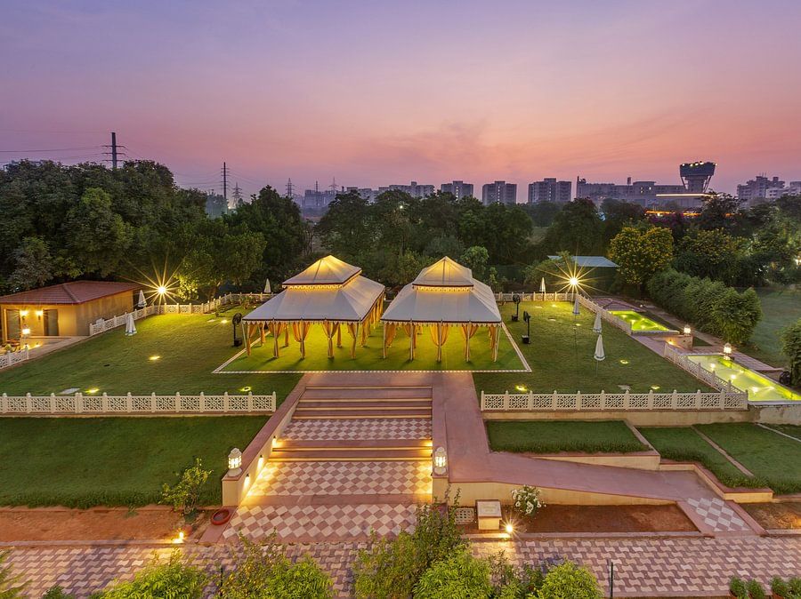 Illuminated tents on a green lawn surrounded by trees under a dusky pink sky - Heritage Village Resorts & Spa.