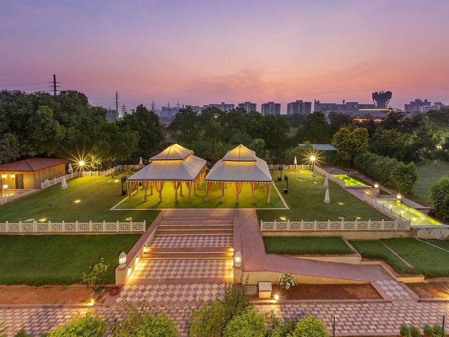 Illuminated tents on a green lawn surrounded by trees under a dusky pink sky - Heritage Village Resorts & Spa.