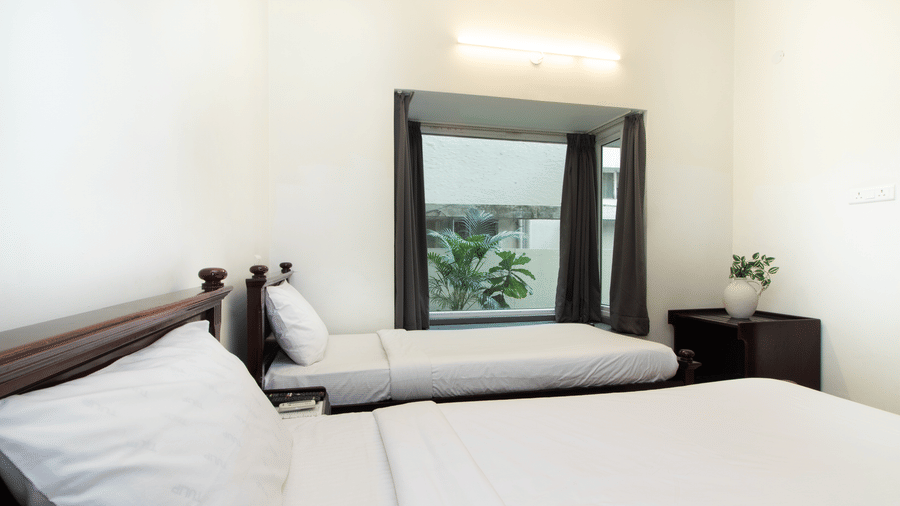Hotel room with a double bed, a wall mirror, and a window with greenery views at Sanctum Suites Indiranagar, Bangalore.