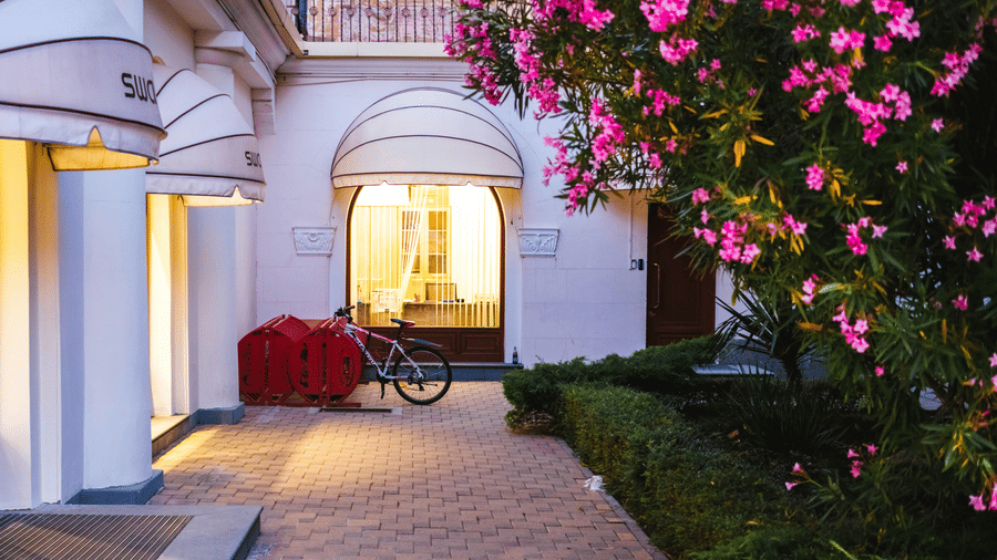 The exterior of a boutique shop with white awnings, a bike and a red cart outside, and vibrant pink flowering bushes.