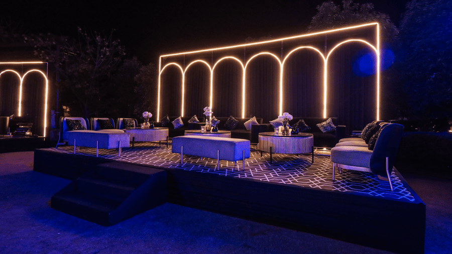 Chic outdoor event lounge at Ananta Spa & Resort, Jaipur, with a raised platform and arch-shaped neon-style lighting backdrop.