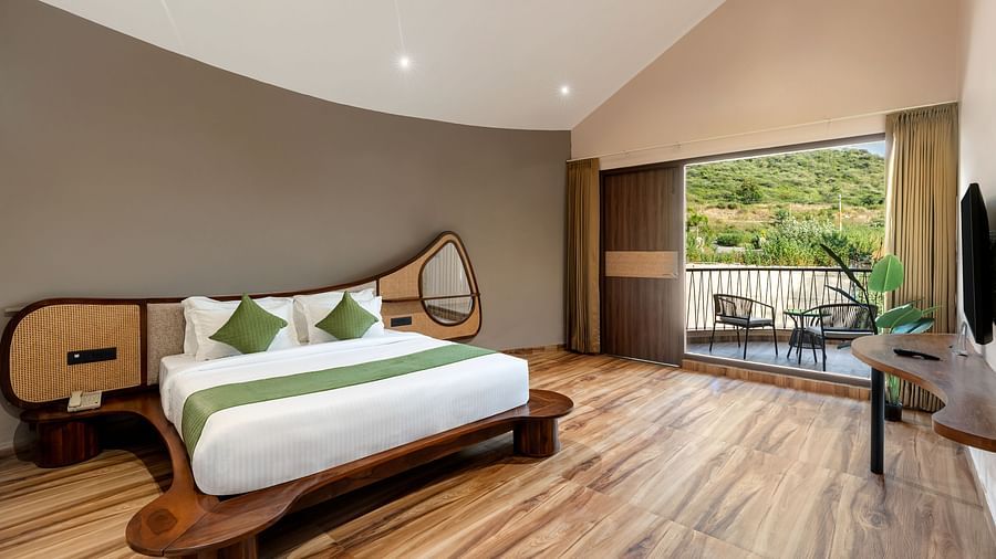 Luxury Villa with Sitout showcasing a king size bed with green accents, wooden flooring, and a view of the outdoors through a large window at The Qualia Resort Club & Brewery, Udaipur.