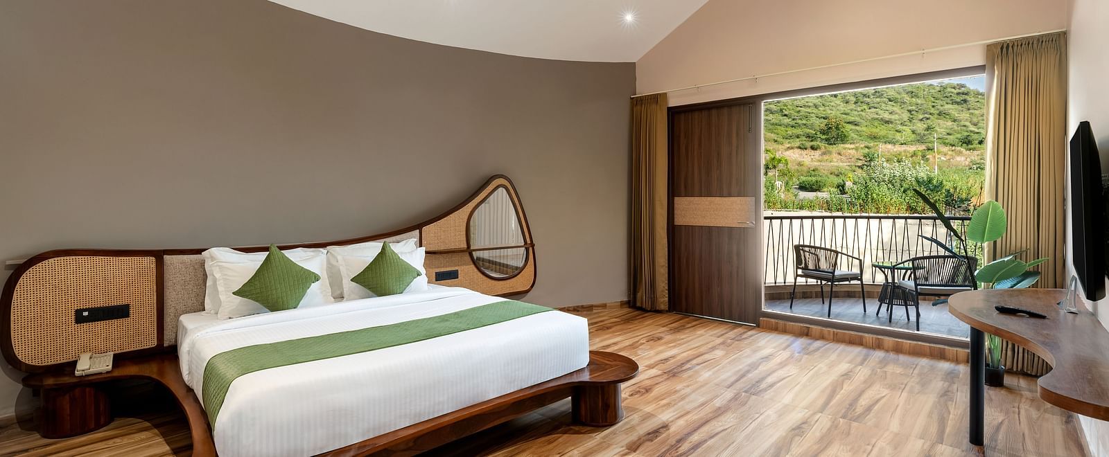 Luxury Villa with Sitout showcasing a king size bed with green accents, wooden flooring, and a view of the outdoors through a large window at The Qualia Resort Club & Brewery, Udaipur.