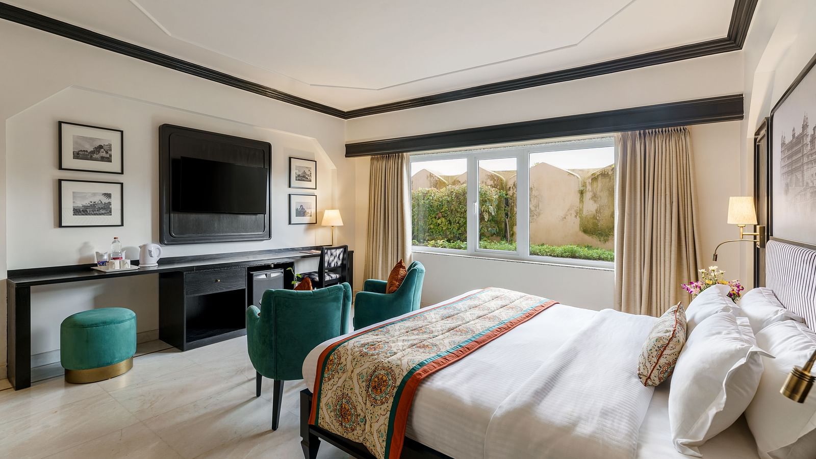  a king bed in one of our spacious rooms in Udaipur featuring two green sofas, a TV, a wardrobe and several wall paintings - Hotel Rajdarshan, Udaipur.