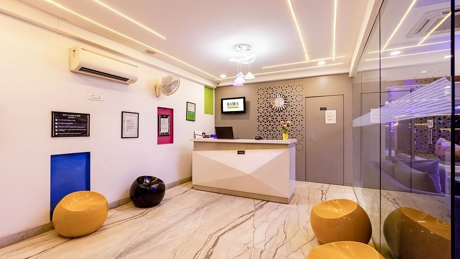 Hotel reception area with a desk, stools, and framed art on the wall at Hotel Bawa, Gurgaon.