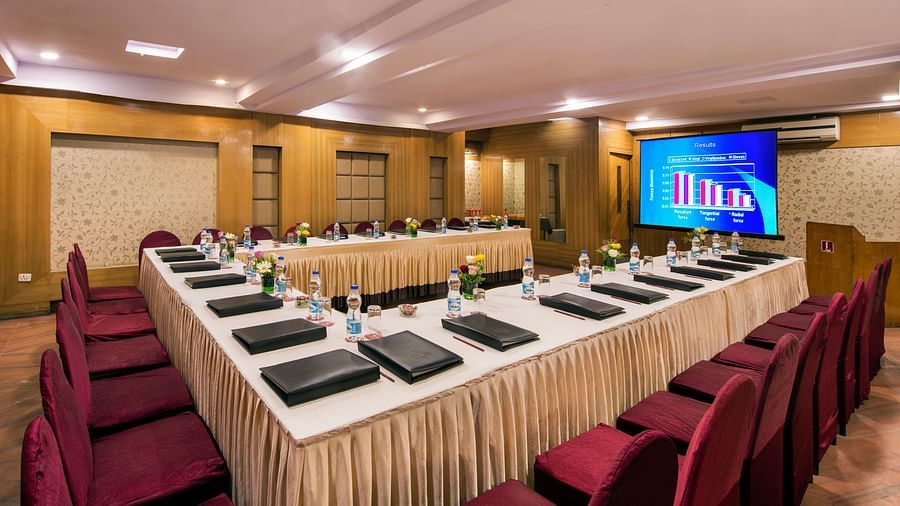 A hotel conference room with long tables, chairs, and a screen displaying Arabic text - Lords Eco Inn Dahej
