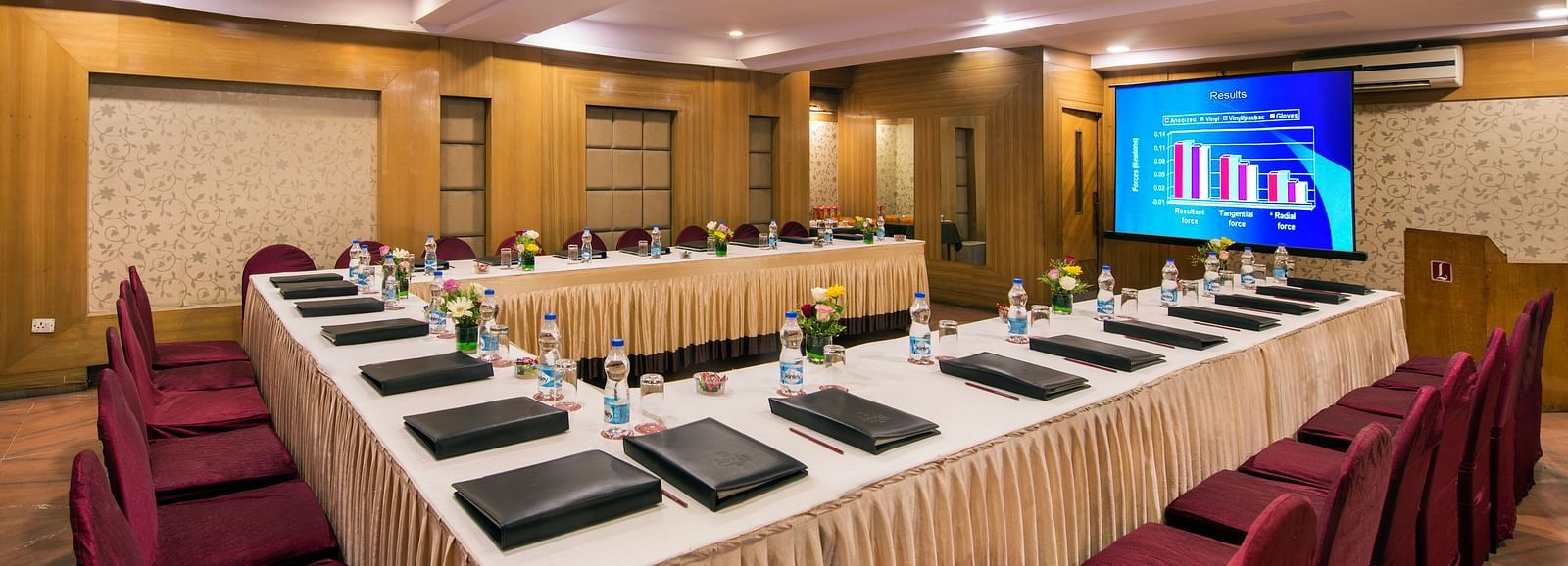 A hotel conference room with long tables, chairs, and a screen displaying Arabic text - Lords Eco Inn Dahej