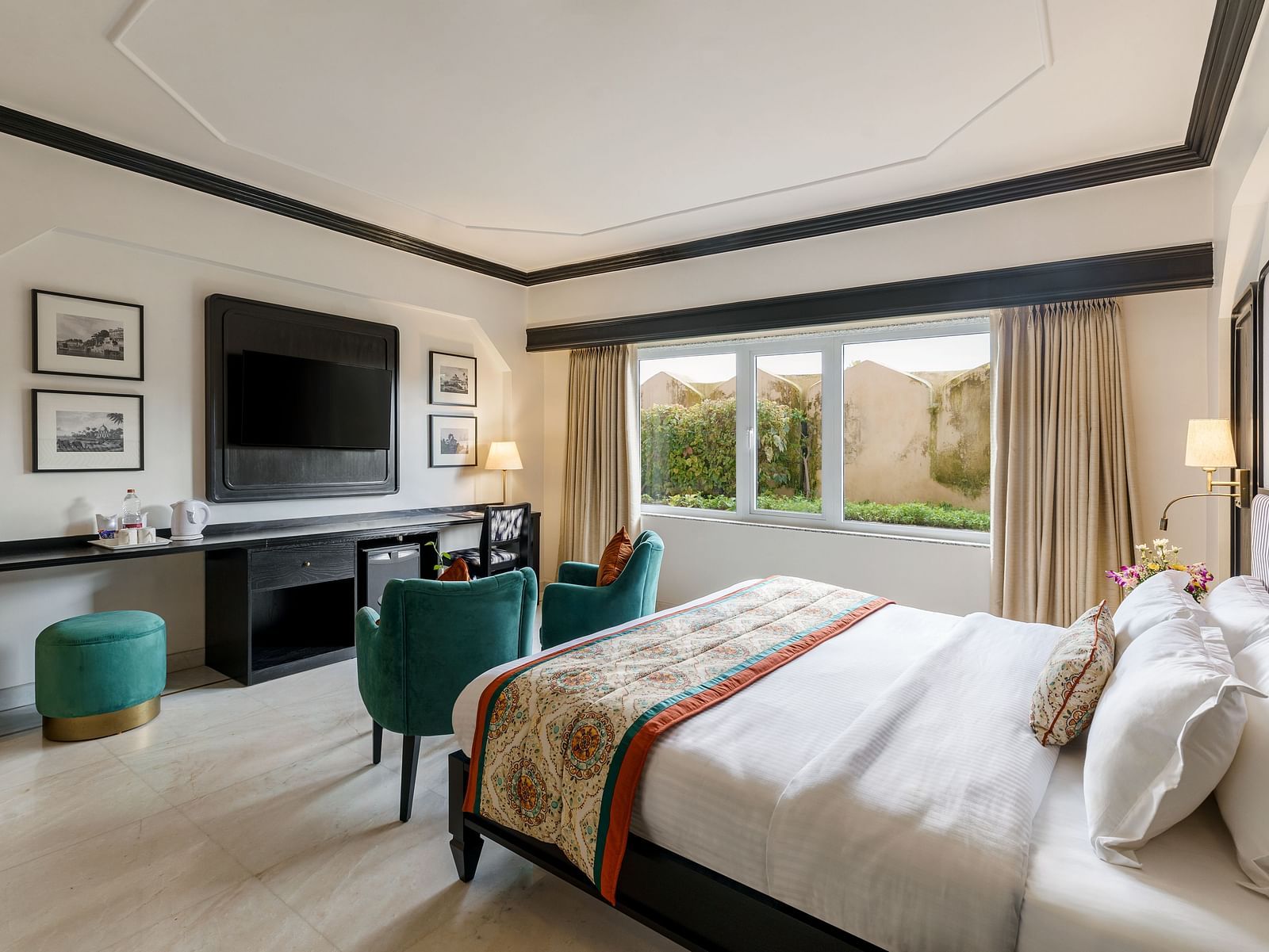  a king bed in one of our spacious rooms in Udaipur featuring two green sofas, a TV, a wardrobe and several wall paintings - Hotel Rajdarshan, Udaipur.