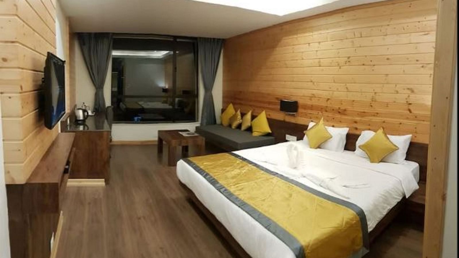 An image of a premium room with a bed, flat screen TV, a couch, table, and an expansive window - Yashshree Sanderling, Darjeeling