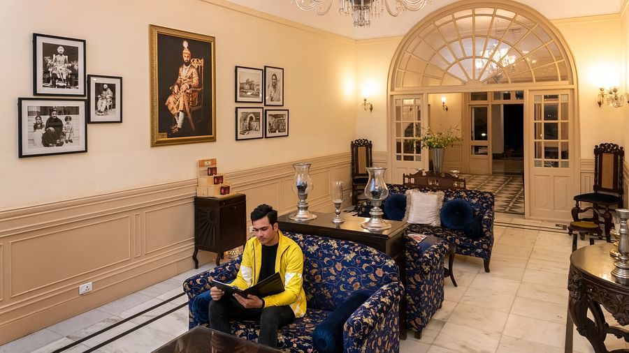 An image of a person sitting in the lobby with navy blue couch sets and filled with photographs of the royal family of Nabha