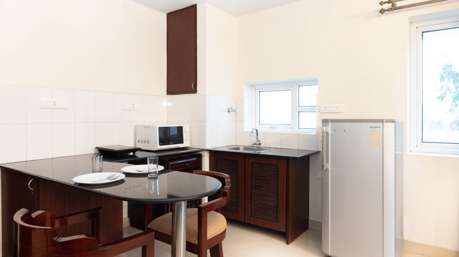 Hotel room with a kitchenette, a refrigerator, and a dining counter with natural light at Sanctum Suites Indiranagar, Bangalore.