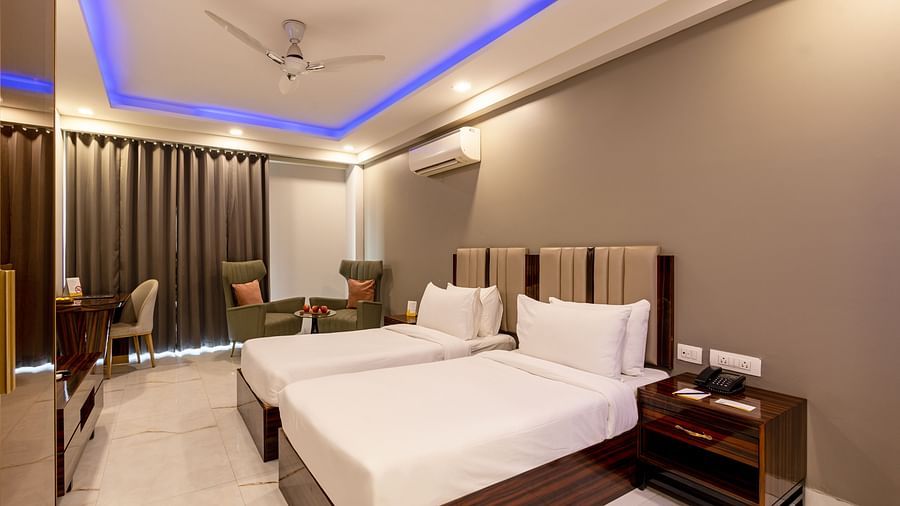 A well-lit room with twin beds and two sofa chairs at Hotel Bawa, Gurgaon.