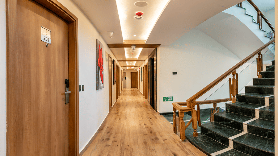 A hotel hallway at Lords Inn Katra featuring wooden room doors, a tiled staircase with a wooden handrail, ceiling panels, and lights.