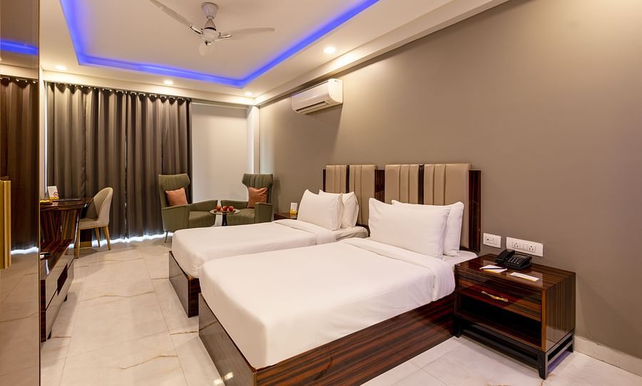 A well-lit room with twin beds and two sofa chairs at Hotel Bawa, Gurgaon.