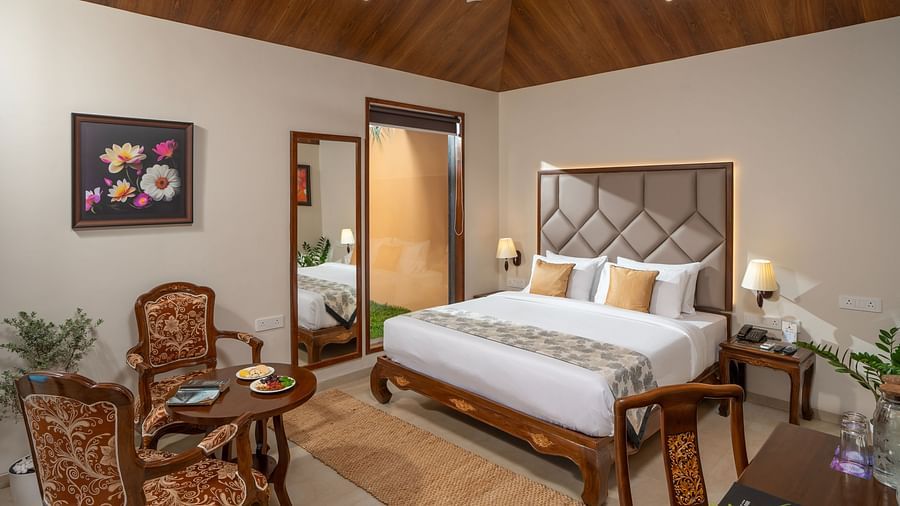 Pool Villa at Uday Backwater Resort featuring a plush bed with a large grey headboard and a sitting space in one corner of the room featuring two wooden chairs and a round coffee table
