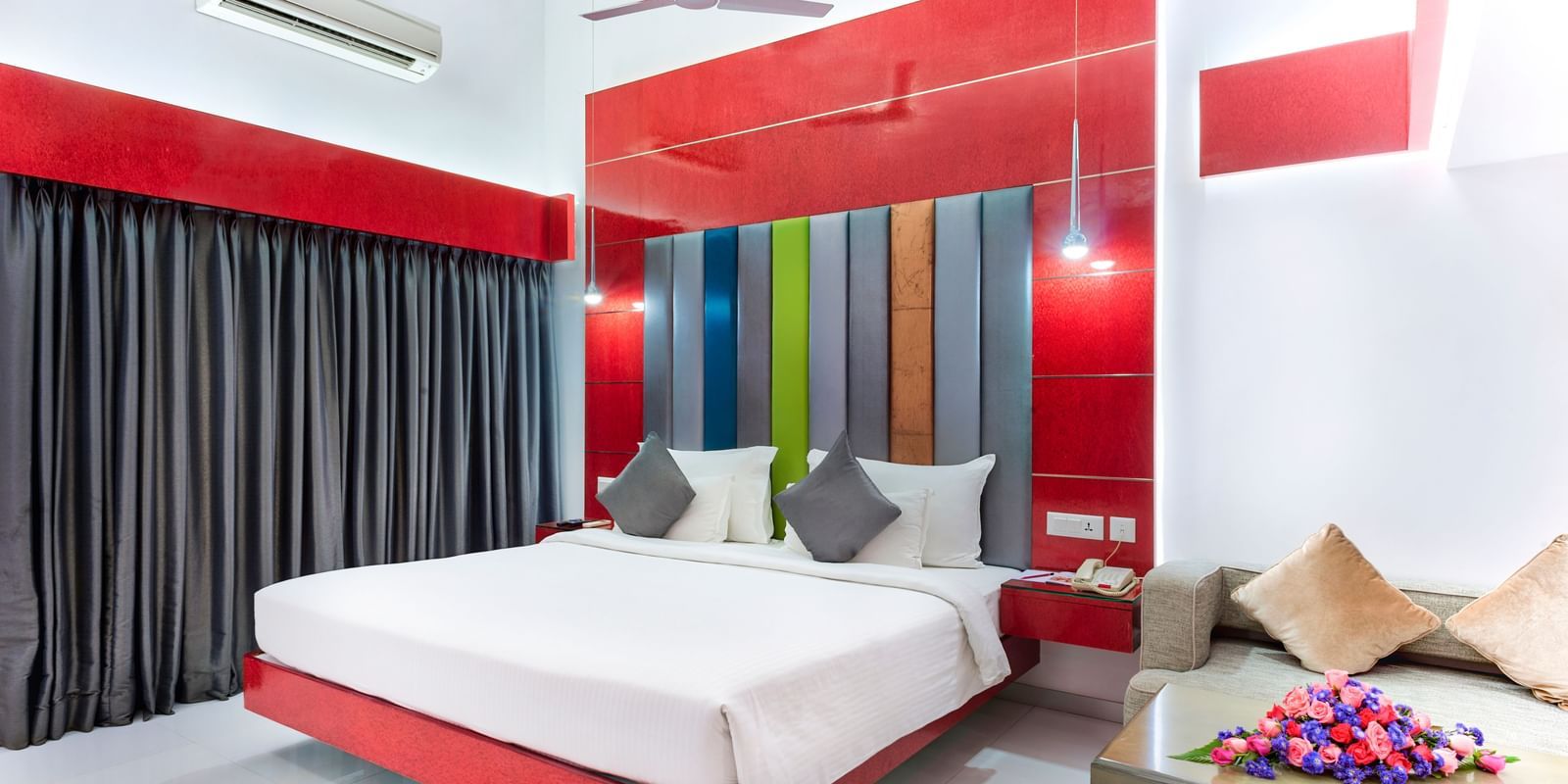 A room with a king size bed featuring colourful wall accents, grey curtains and red & white decor at Grande Bay Resort & Spa.