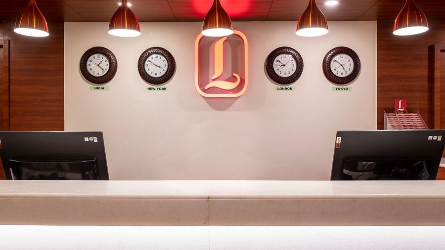 Reception counter with dual stations, ambient lighting, and decorative wall clocks - Lords Eco Inn Shapar Rajkot