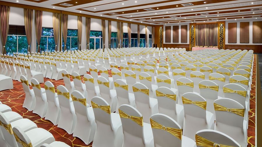 A large conference room set up with rows of white chairs, each adorned with a gold sash at DGV Resort by Treat, Silvassa