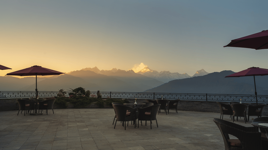An outdoor seating area with tables, chairs, umbrellas, and a view of mountains under a sky during sunset at Summit Norbu Ghang - The Signature Collection, Gangtok.