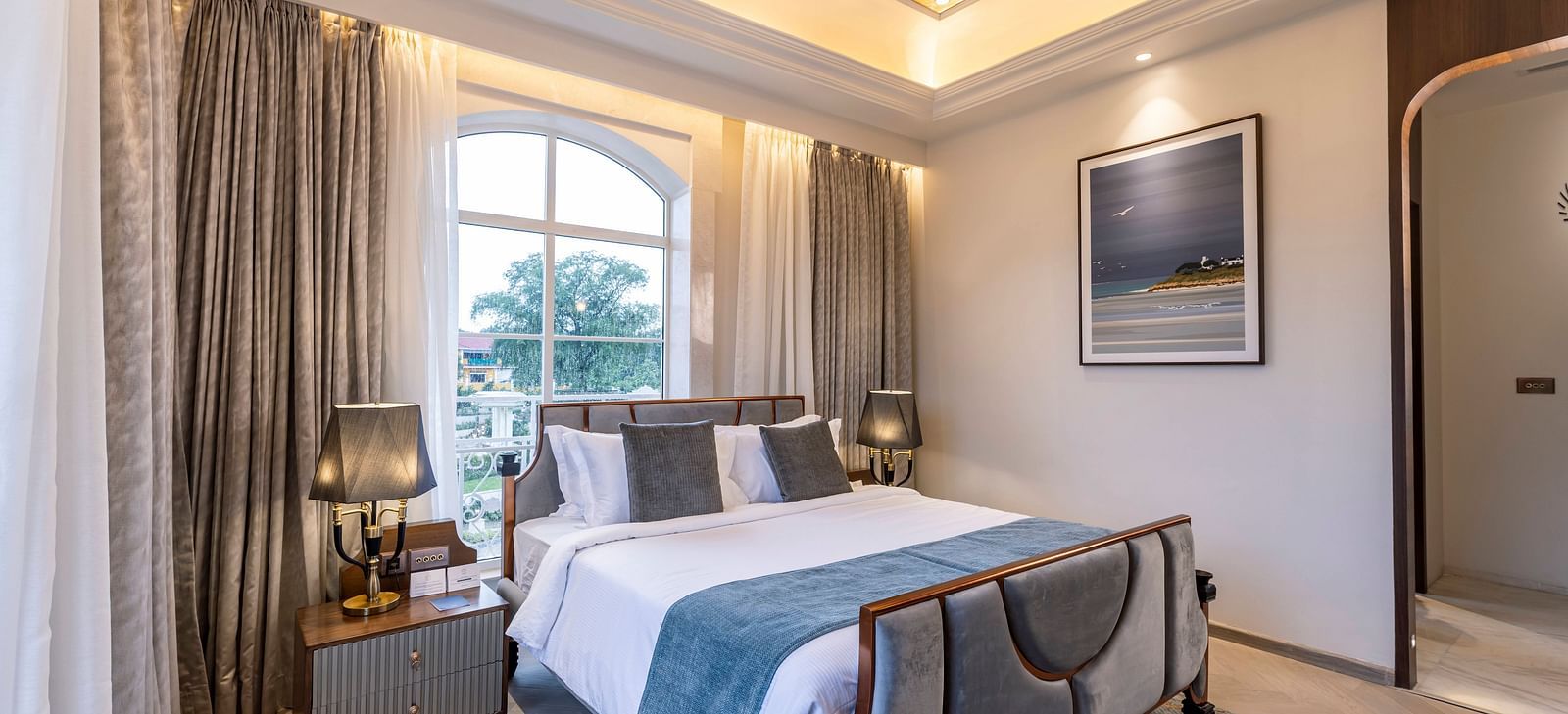 A luxurious bedroom featuring a double bed along with a window with a tree standing tall outside of the Suite at Imperial Goa.