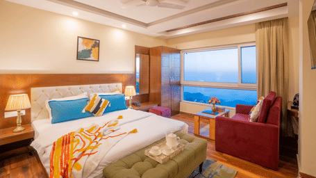 A bedroom with a king size bed, arm chair, large window, curtains, and mountain view visible from inside the room at Perfectstayz Value Valley Vista, Mussoorie.