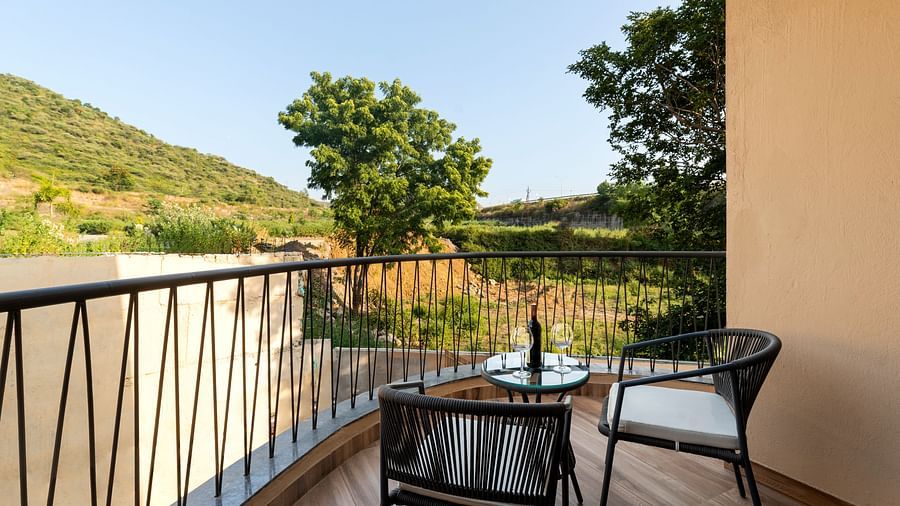 Luxury Villa with Sitout featuring a balcony with a metal railing offers a view of a green landscape, furnished with a small table and chairs at The Qualia Resort Club & Brewery, Udaipur.
