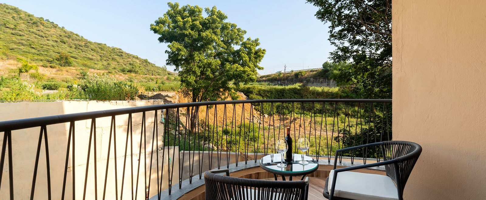 Luxury Villa with Sitout featuring a balcony with a metal railing offers a view of a green landscape, furnished with a small table and chairs at The Qualia Resort Club & Brewery, Udaipur.