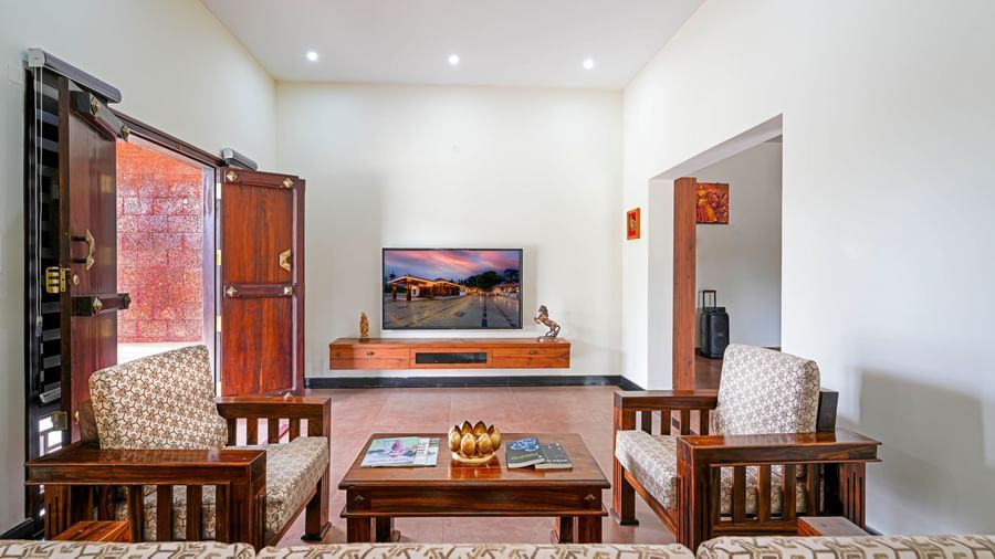 A cozy living area in the villa at Bhuthanakadu Retreat, showcasing a comfortable sofa, a wooden coffee table, and a TV with a stand, all with warm lighting.