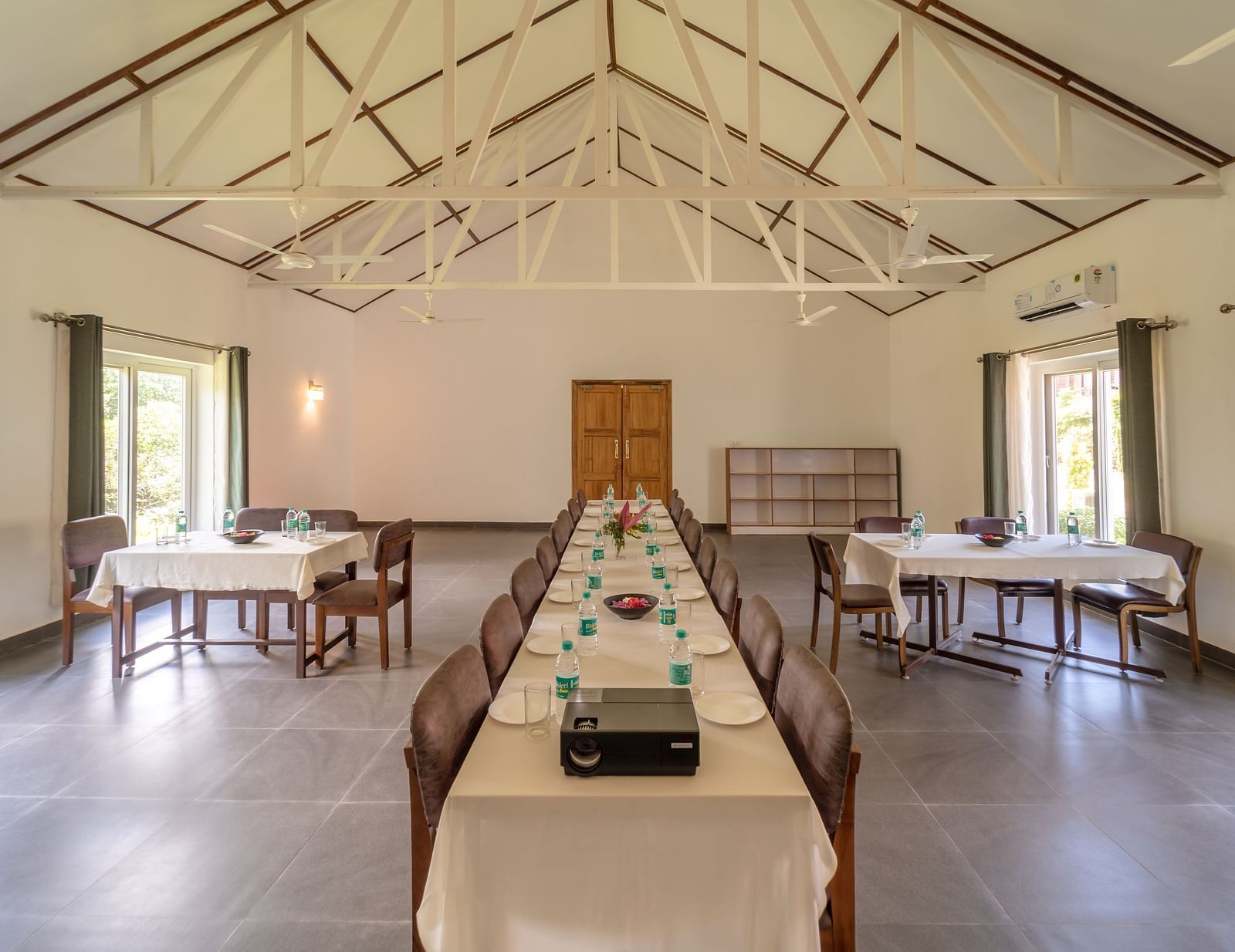 a large dining table in the centre with other small tables on the side inside a room - Neer Ganga Resorts
