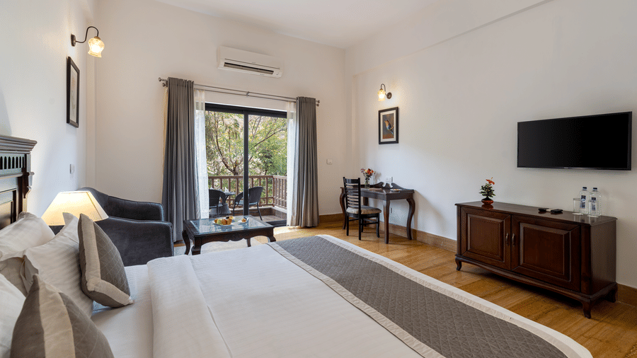 Corner view of the double bed at the brightly lit Hill View Suite With Balcony featuring the french windows that lead to the balcony at The Hunting Lodge, Udaipur.