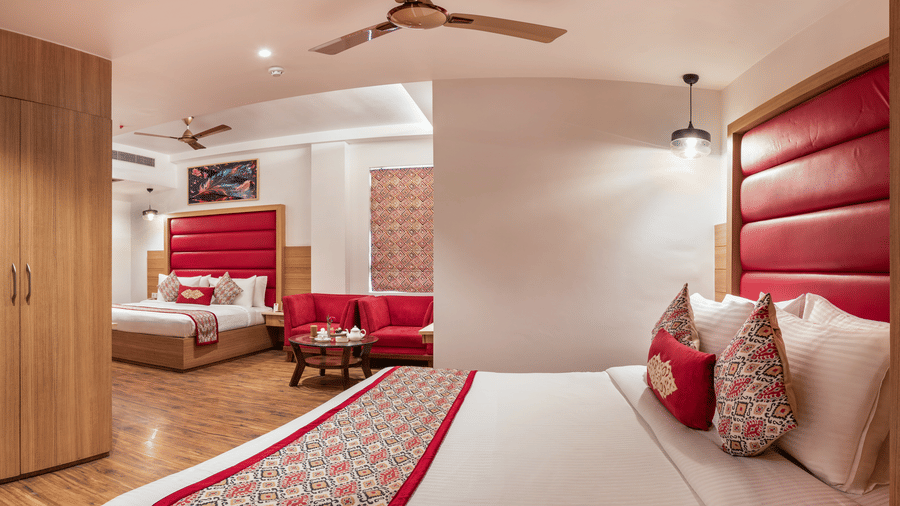 Wide angle view of a Family Room at Lords Inn Amritsar with a king bed, red headboard, wooden flooring, ceiling fan, and warm ambient lighting.