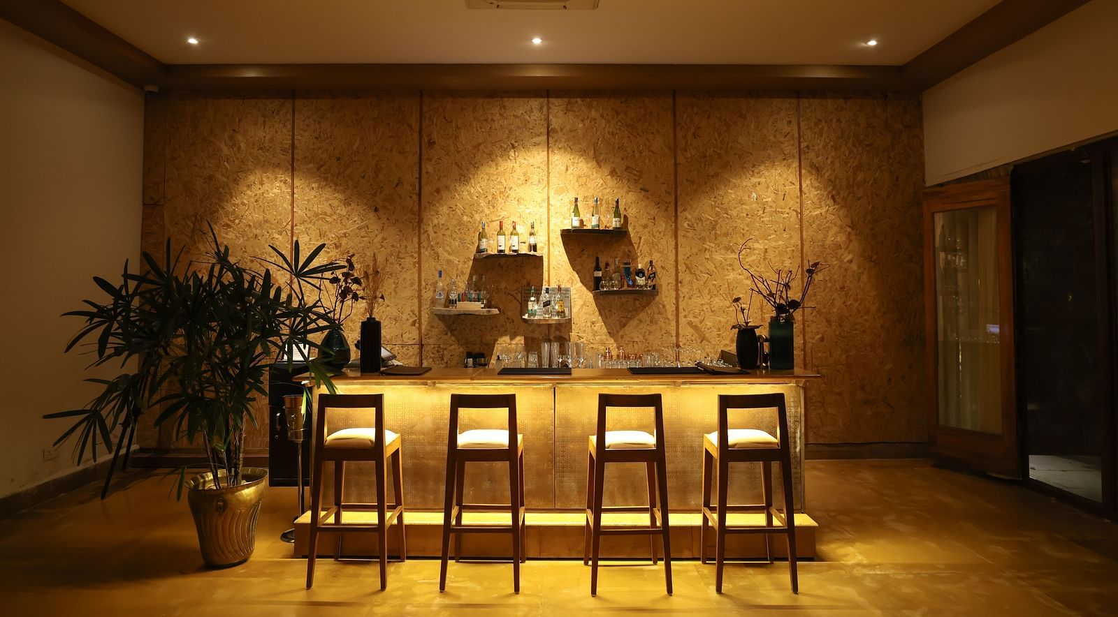 The bar counter at Saraca Bar at Saraca Resort & Spa Corbett with a warm ambience, spot lighting on the chairs and indoor plants placed besides it