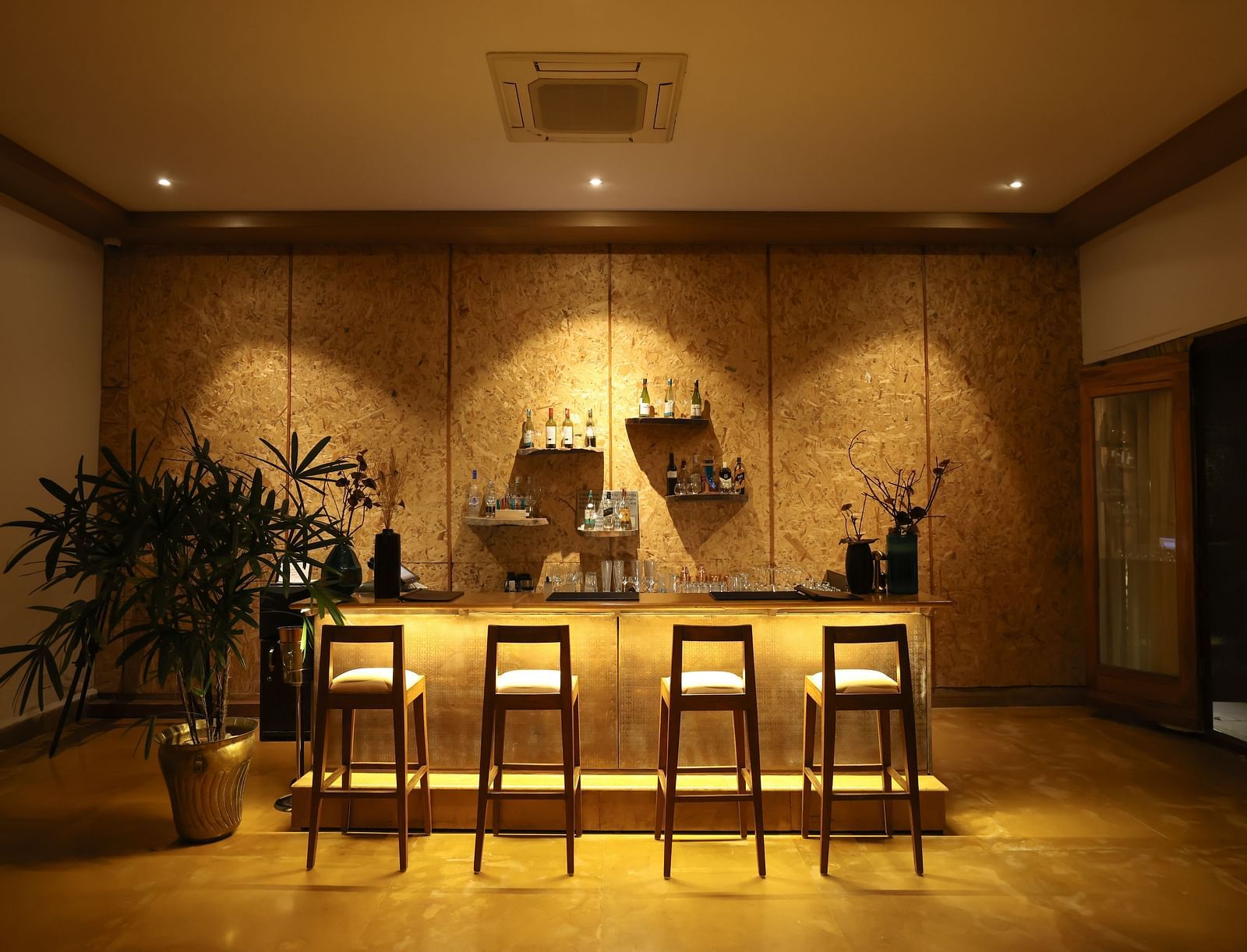 The bar counter at Saraca Bar at Saraca Resort & Spa Corbett with a warm ambience, spot lighting on the chairs and indoor plants placed besides it