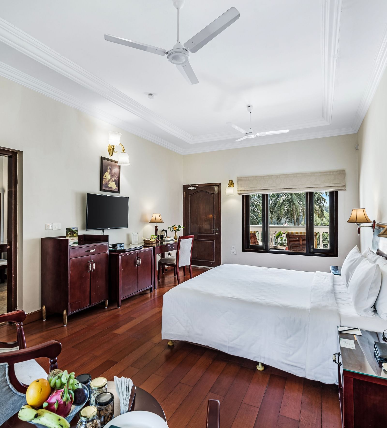 An image of the Garden room with river view featuring a queen size bed, bed side tables, lamps, ceiling fan, flat screen TV, and chairs - GReaT Trails River View Resort Thanjavur By GRT Hotels