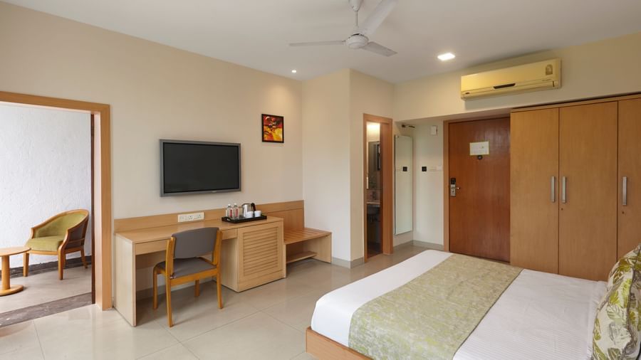 A spacious hotel room at Monday Hotels Mahape, Navi Mumbai, showing the bed, a desk, and the bathroom entrance.