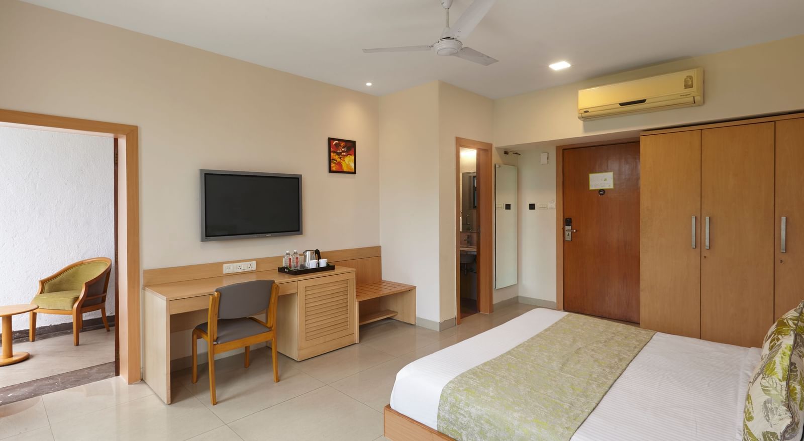 A spacious hotel room at Monday Hotels Mahape, Navi Mumbai, showing the bed, a desk, and the bathroom entrance.