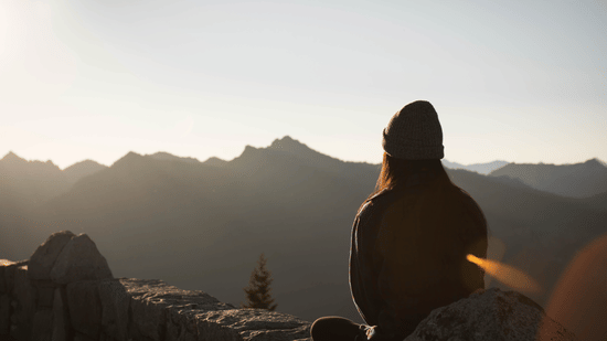 silhouette of woman sitting on a mountain peak