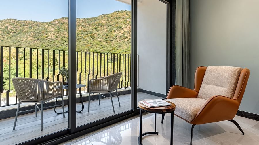Club Suite with Valley View Sitout with a balcony with outdoor seating, offering views of mountains and greenery through large glass doors at The Qualia Resort Club & Brewery, Udaipur.