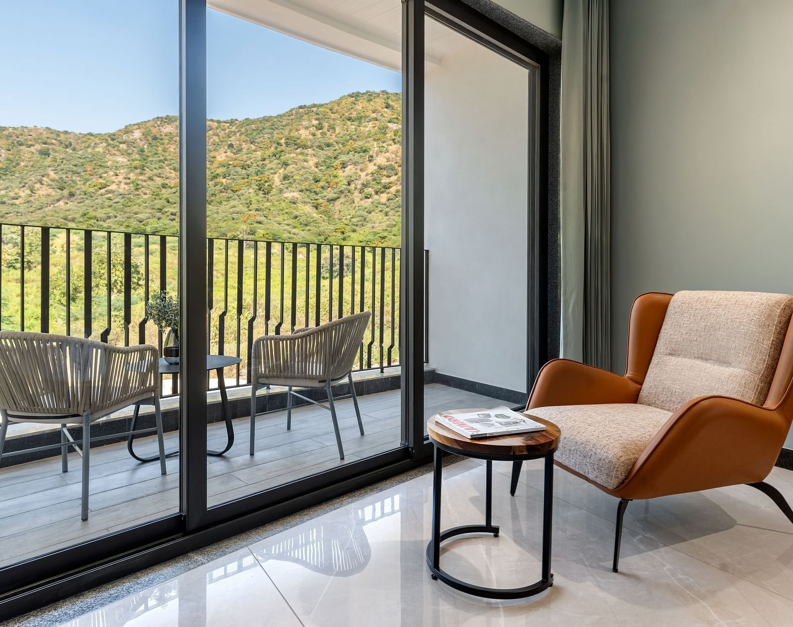 Club Suite with Valley View Sitout with a balcony with outdoor seating, offering views of mountains and greenery through large glass doors at The Qualia Resort Club & Brewery, Udaipur.