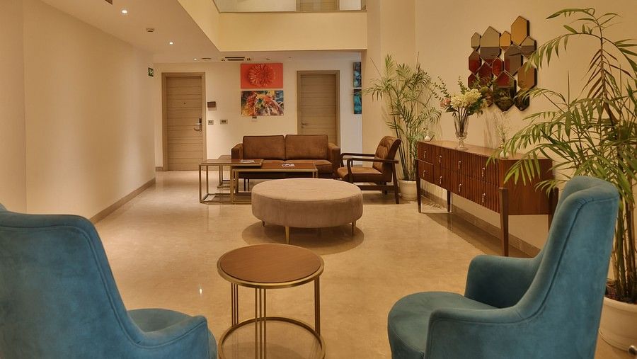 Spacious lobby seating area with blue chairs, plants, and bright lighting at Hotel Saket 27. 