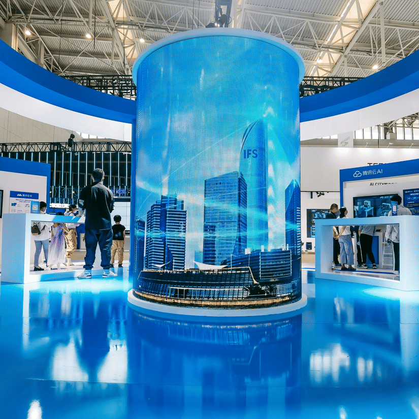A view from inside an exhibition stall with a central installation and blue flooring and a person standing at the far end.