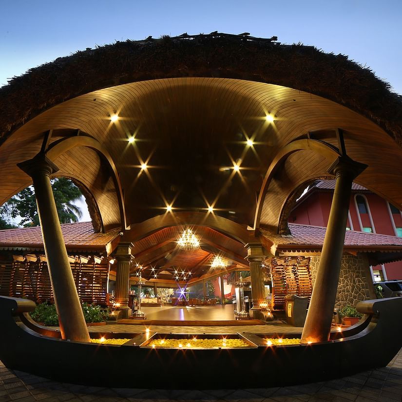 The illuminated entrance of Uday Samudra Leisure Beach Hotel in Kovalam featuring a boat-shaped water feature and warm lighting at dusk