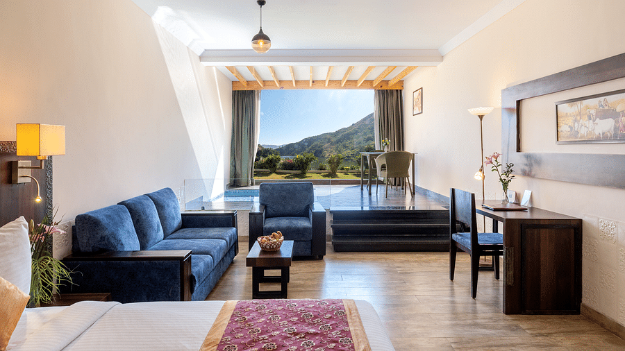 A living area with a blue couch, a neatly arranged bed, and a window with mountain view - Via Lakhela Resort & Spa