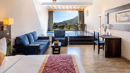 A living area with a blue couch, a neatly arranged bed, and a window with mountain view - Via Lakhela Resort & Spa