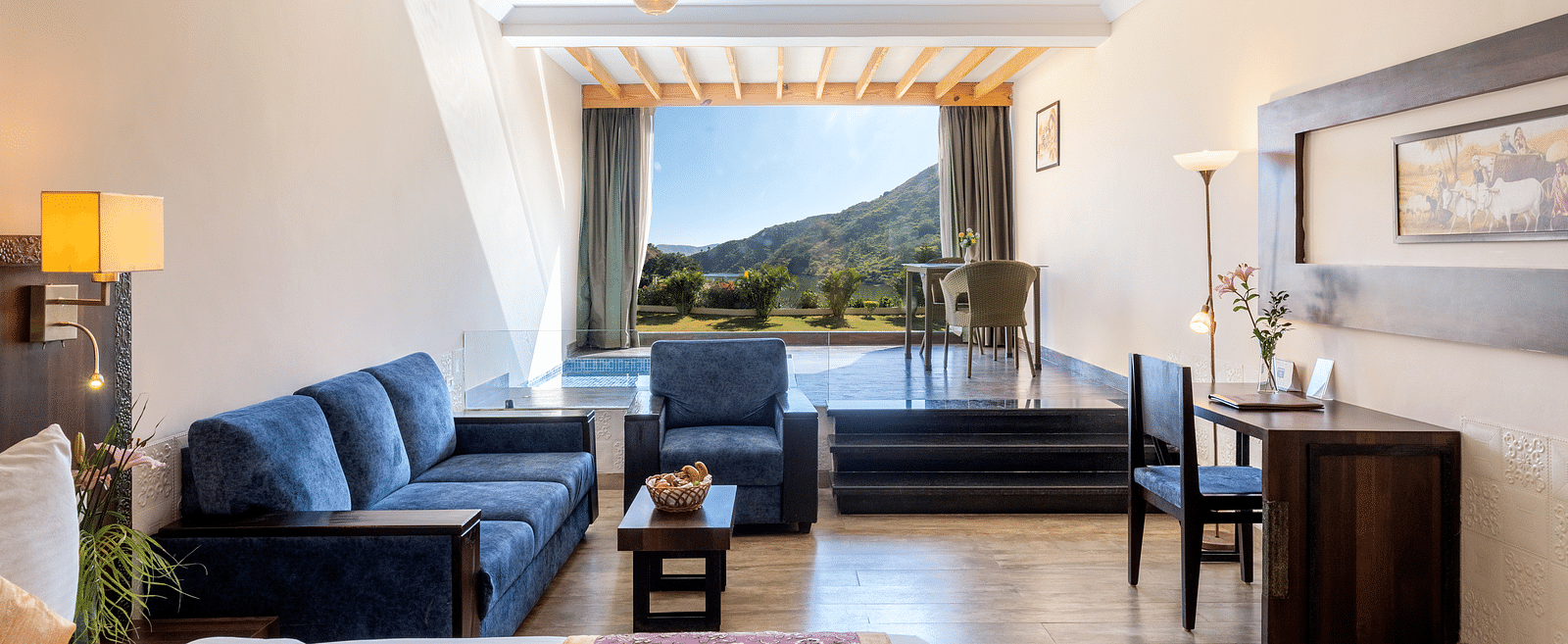 A living area with a blue couch, a neatly arranged bed, and a window with mountain view - Via Lakhela Resort & Spa